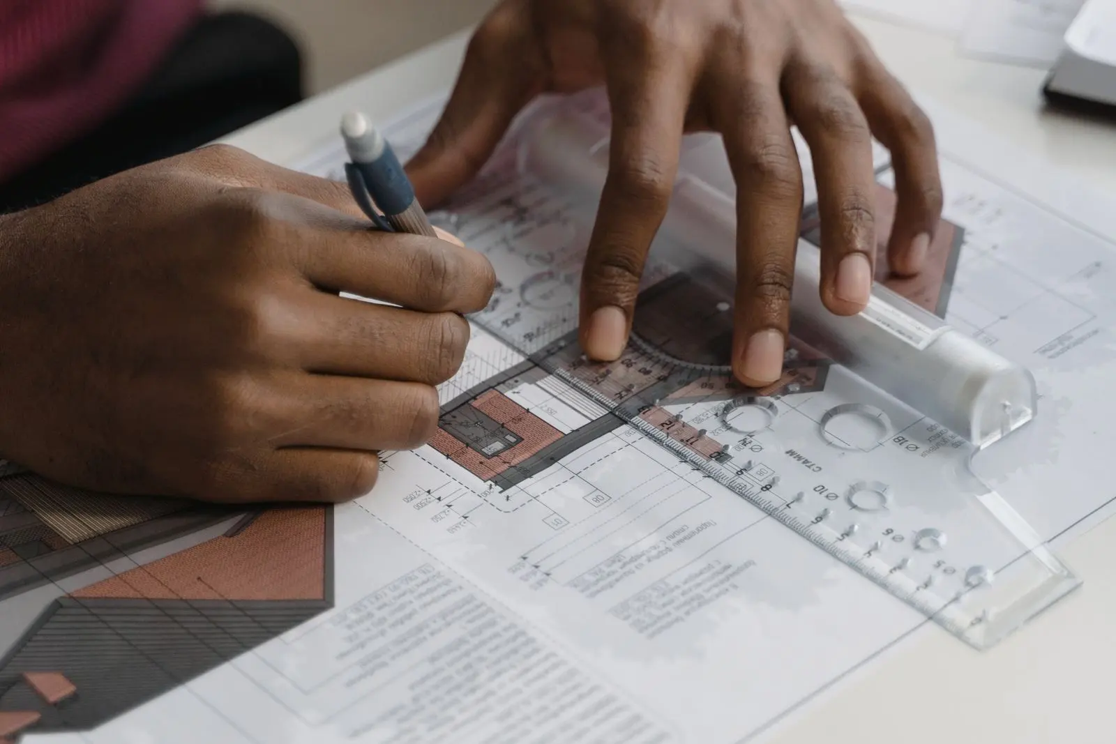 Hands drafting a house floor plan with ruler and pencil — design planning reference